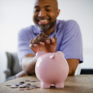 Smiling black man putting coins in piggy bank
